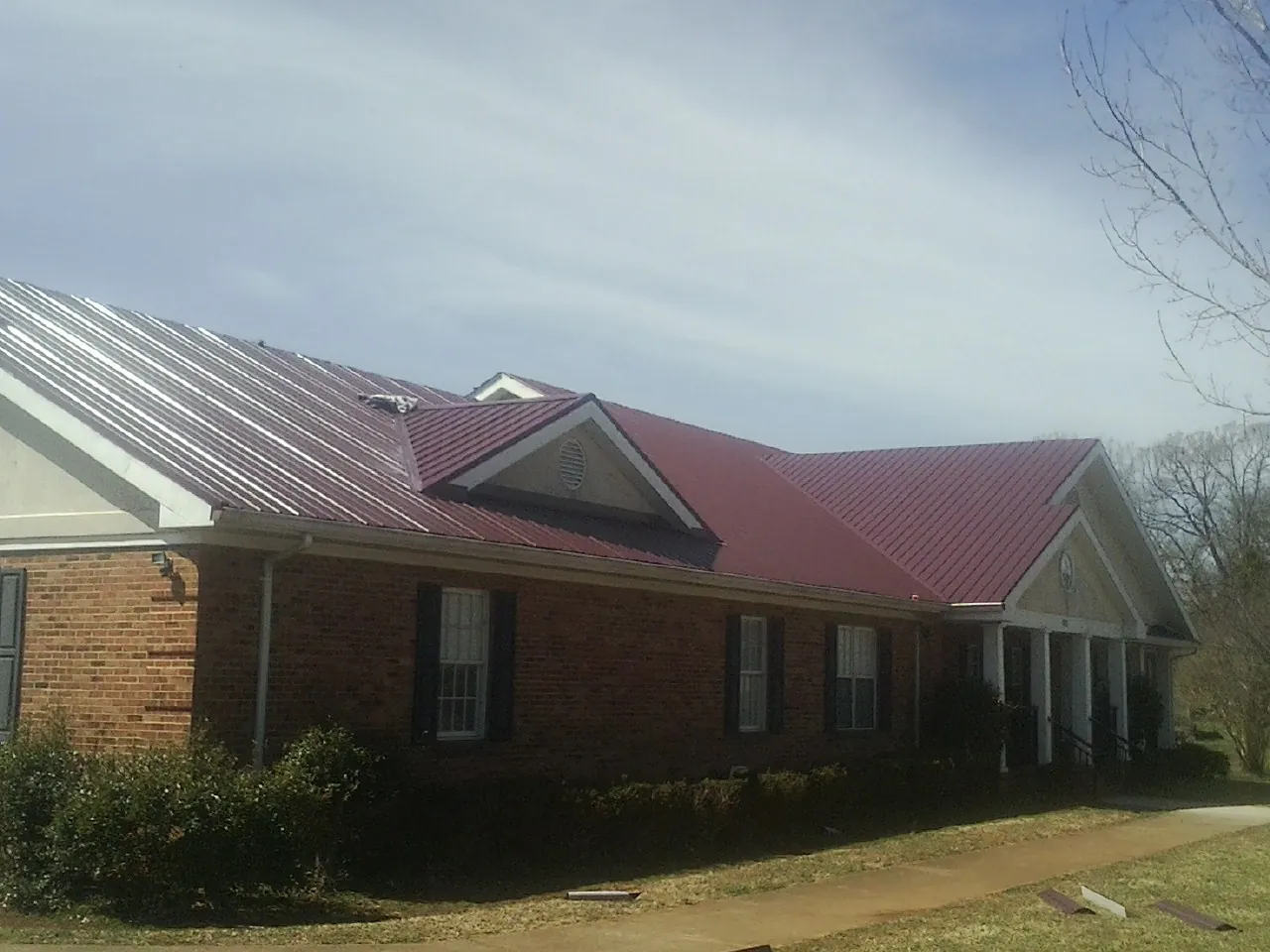 Red metal roof with gabled entries on a long brick building, from a Hail Damage Roof Repair job in Miramar Beach