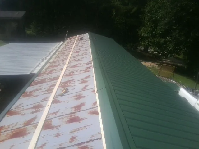 Old rusted panels beside newly installed green metal roofing — Wind Damage Roof Repair by Roofing Brothers in Miramar Beach