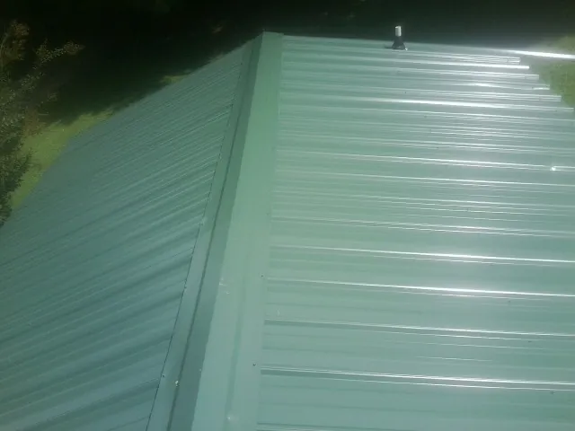 New green metal panels meeting at the ridge of a roof — Flat Roof Repair work by our crew in Miramar Beach