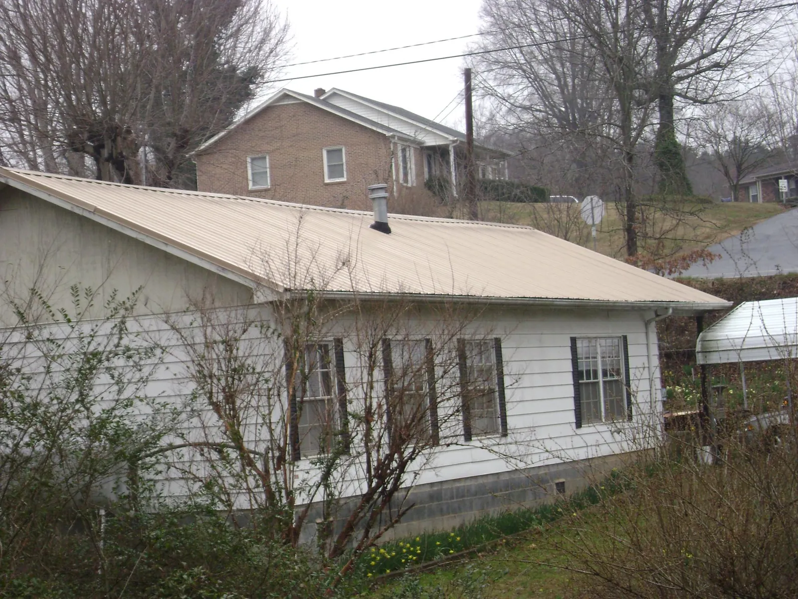 Tan metal roof on a white sided house set into a hillside — Commercial Roofing by Roofing Brothers in Miramar Beach