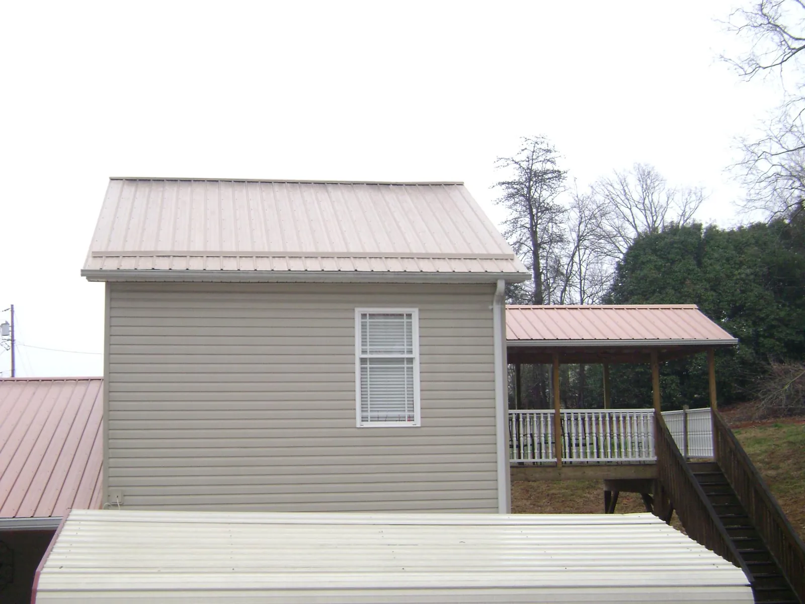 Tan metal roofs on a two story addition and attached porch, from a Roof Replacement job in Miramar Beach
